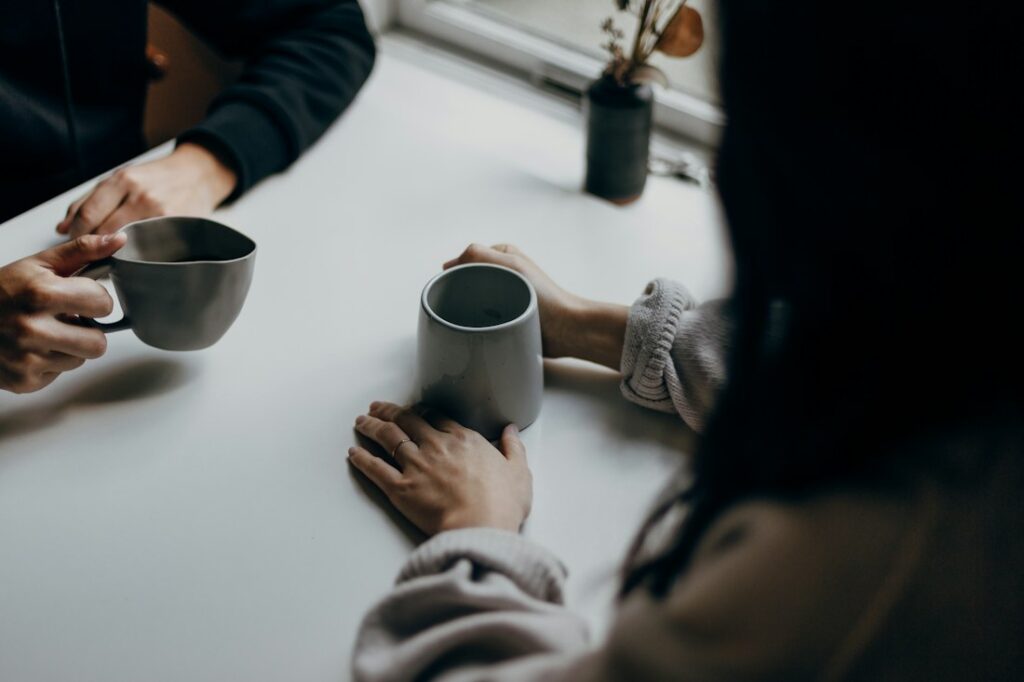 Twee mensen praten met een kop koffie aan tafel; sfeerbeeld